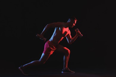 Photo of Man exercising with dumbbells in red light on black background