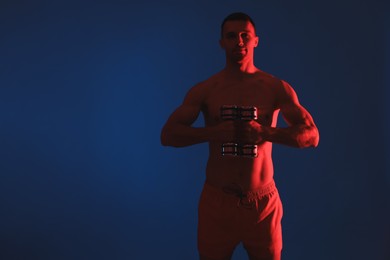 Photo of Man exercising with dumbbells in red light on blue background. Space for text