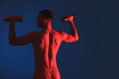 Photo of Man exercising with dumbbells in red light on blue background, back view