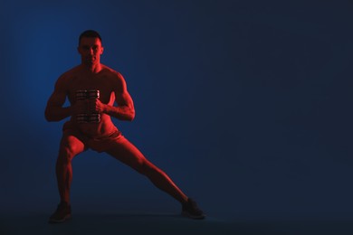 Photo of Man exercising with dumbbells in red light on blue background, space for text