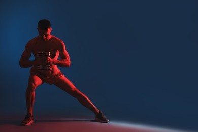 Photo of Man exercising with dumbbells in red light on blue background, space for text