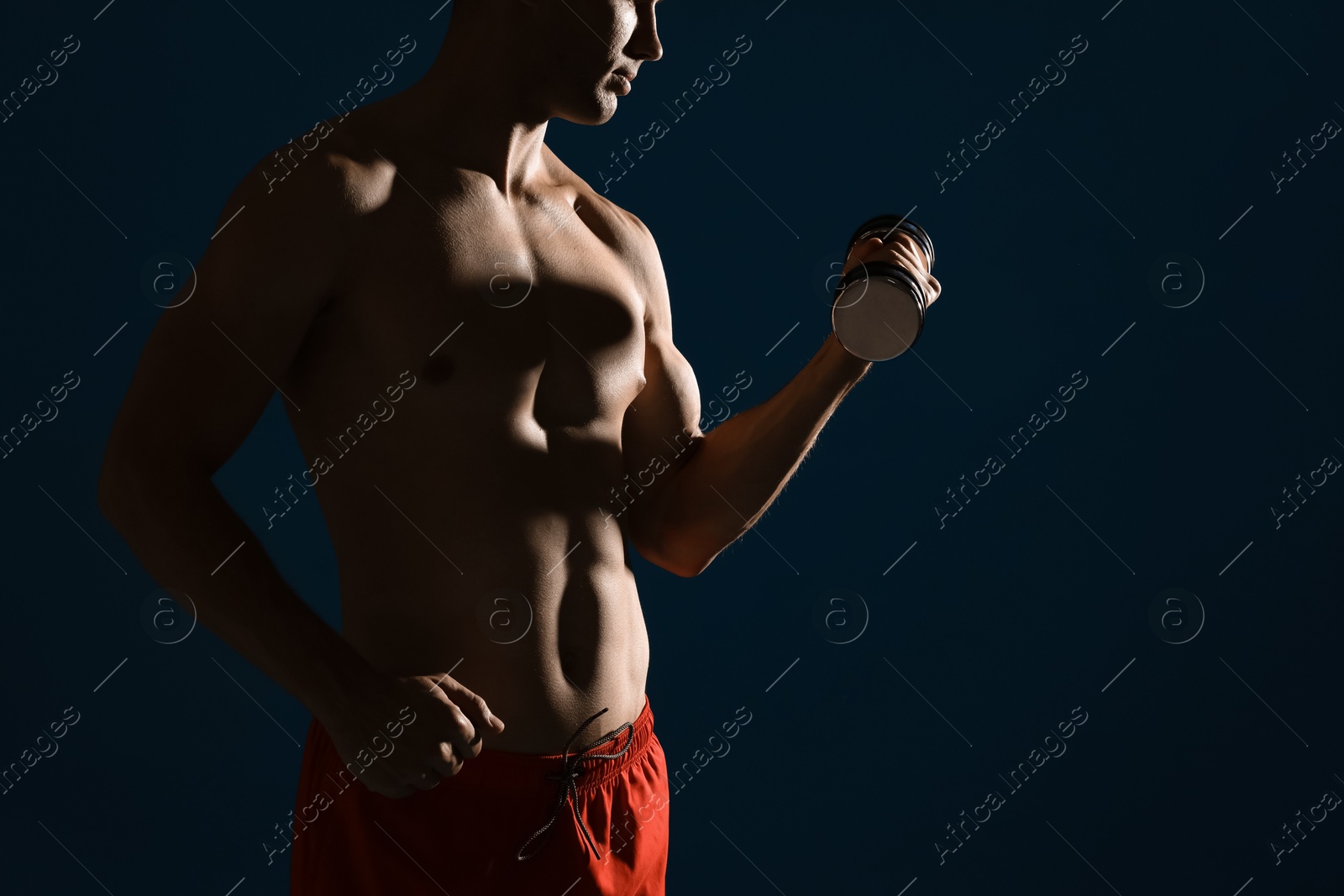 Photo of Man exercising with dumbbell on dark blue background, closeup