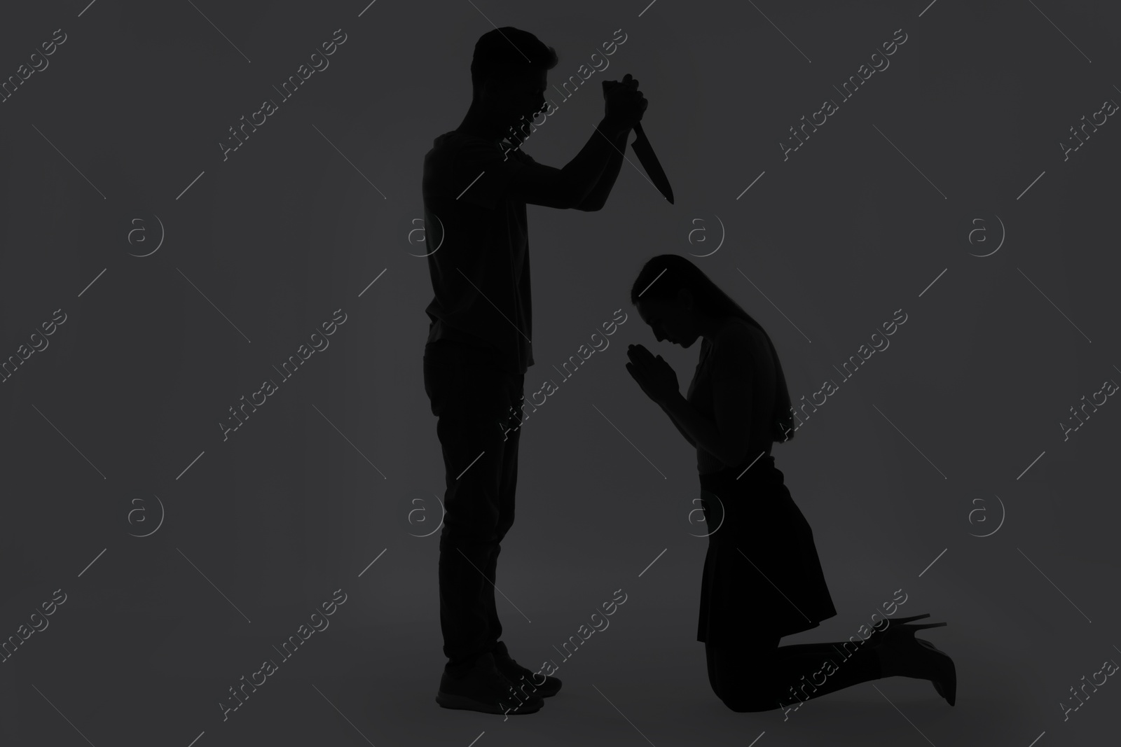 Photo of Domestic violence. Silhouette of man with knife threatening his wife on grey background