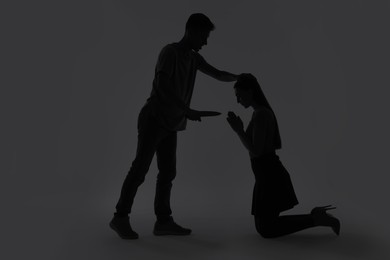 Photo of Domestic violence. Silhouette of man with knife threatening his wife on grey background