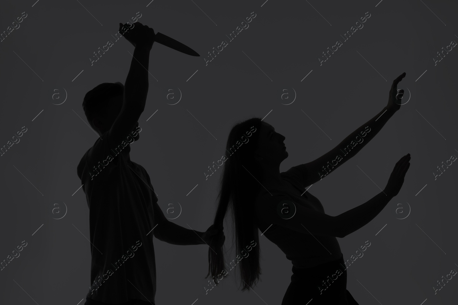 Photo of Domestic violence. Silhouette of man with knife trying to kill his wife on grey background