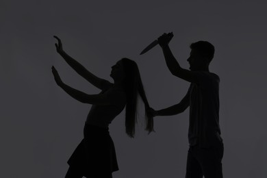 Photo of Domestic violence. Silhouette of man with knife trying to kill his wife on grey background