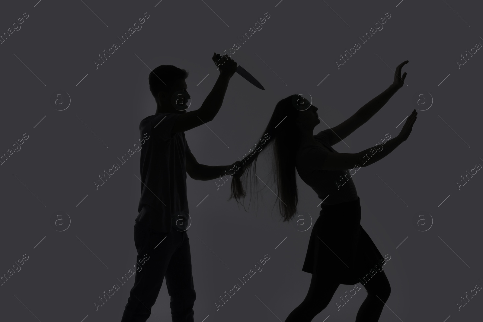 Photo of Domestic violence. Silhouette of man with knife trying to kill his wife on grey background