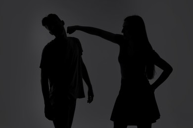 Photo of Domestic violence. Silhouette of woman punching her husband on grey background