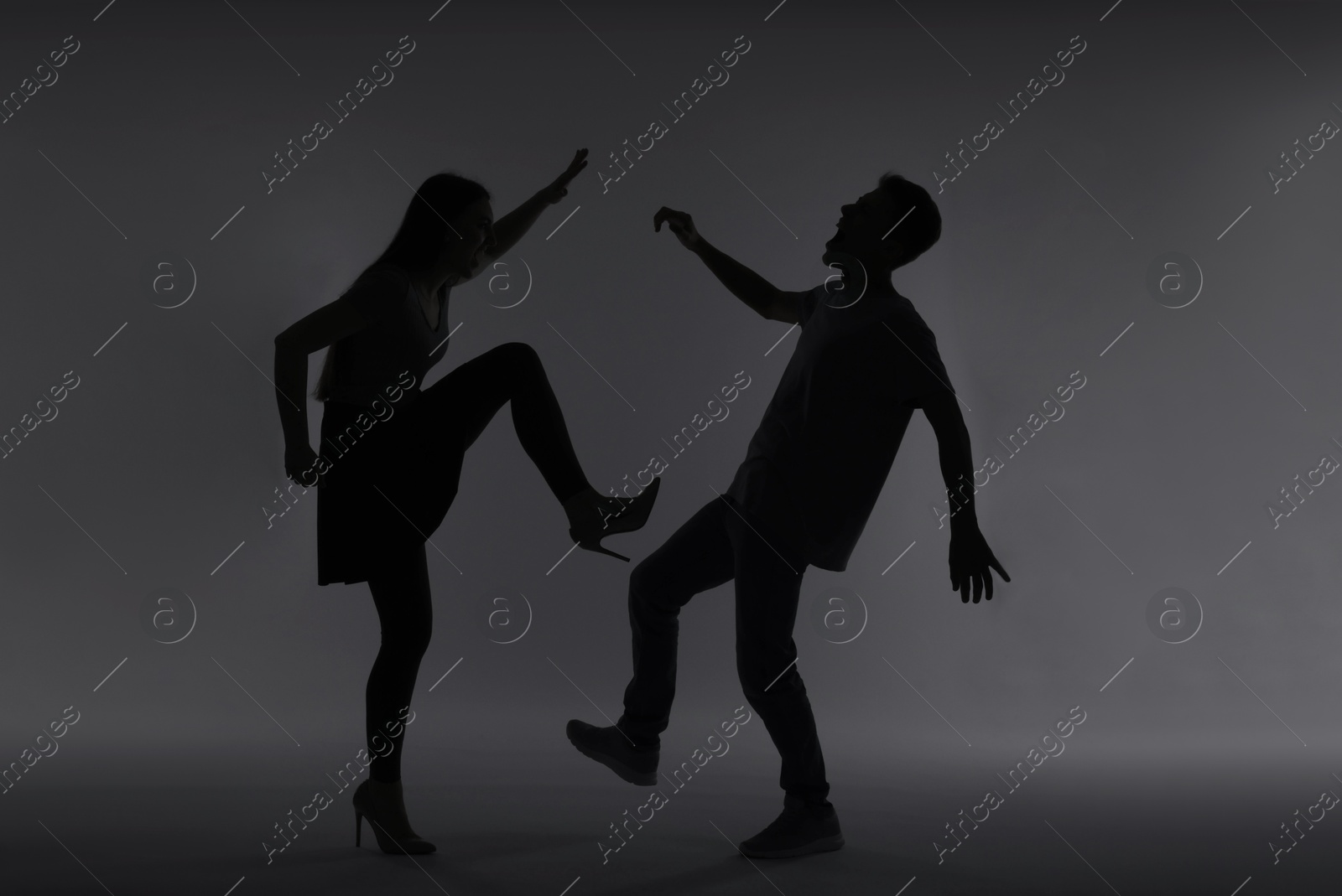 Photo of Domestic violence. Silhouette of woman kicking her husband on grey background