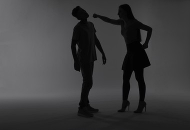 Photo of Domestic violence. Silhouette of woman punching her husband on grey background