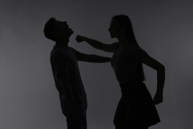 Photo of Domestic violence. Silhouette of woman punching her husband on grey background