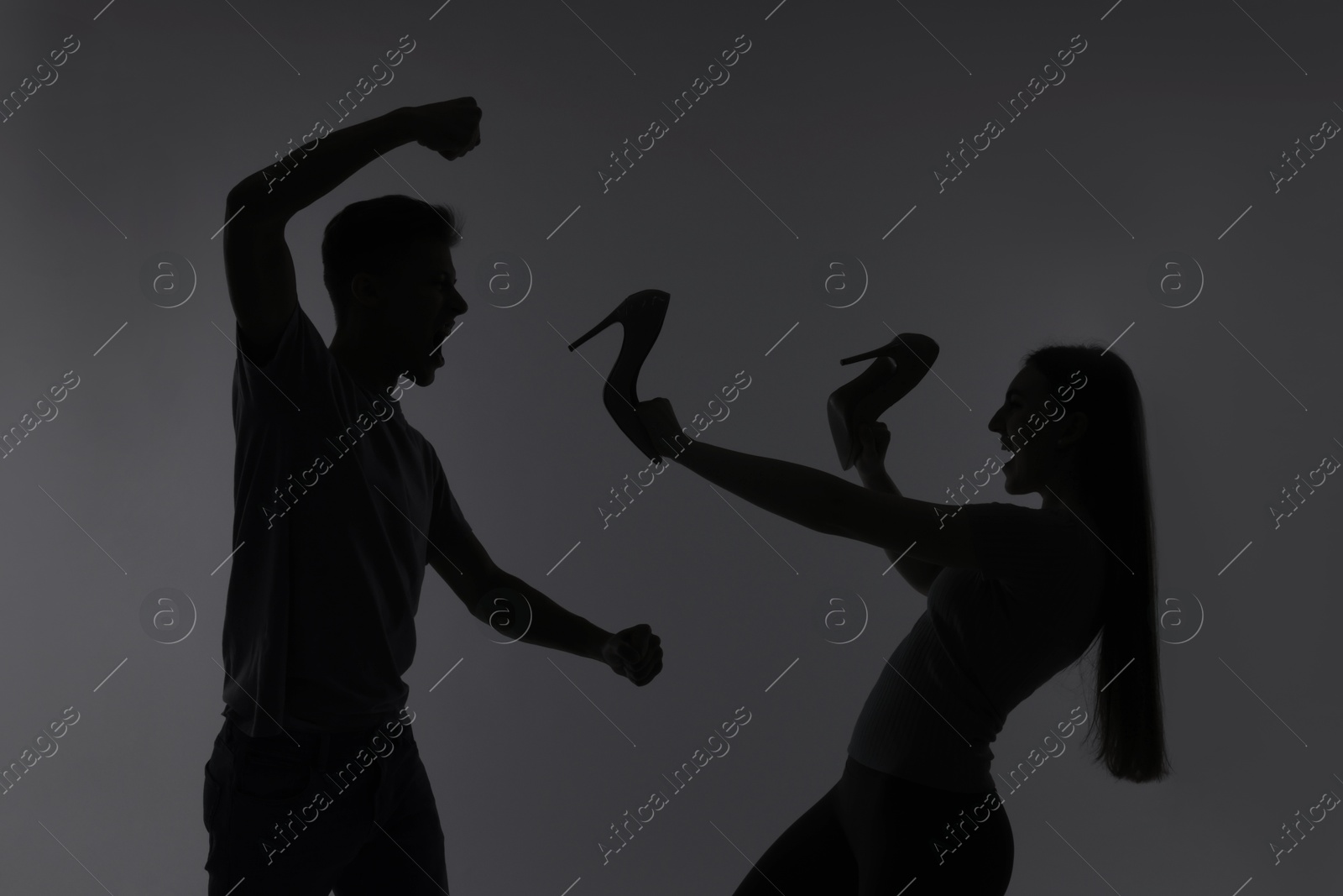 Photo of Domestic violence. Silhouette of man threatening his wife on grey background