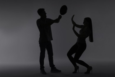 Photo of Domestic violence. Silhouette of man with frying pan threatening his wife on grey background