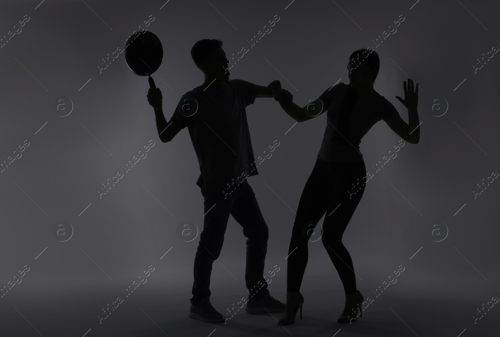 Photo of Domestic violence. Silhouette of man with frying pan threatening his wife on grey background