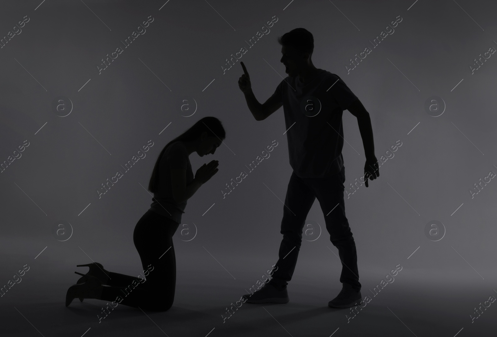 Photo of Domestic violence. Silhouette of man threatening his wife on grey background