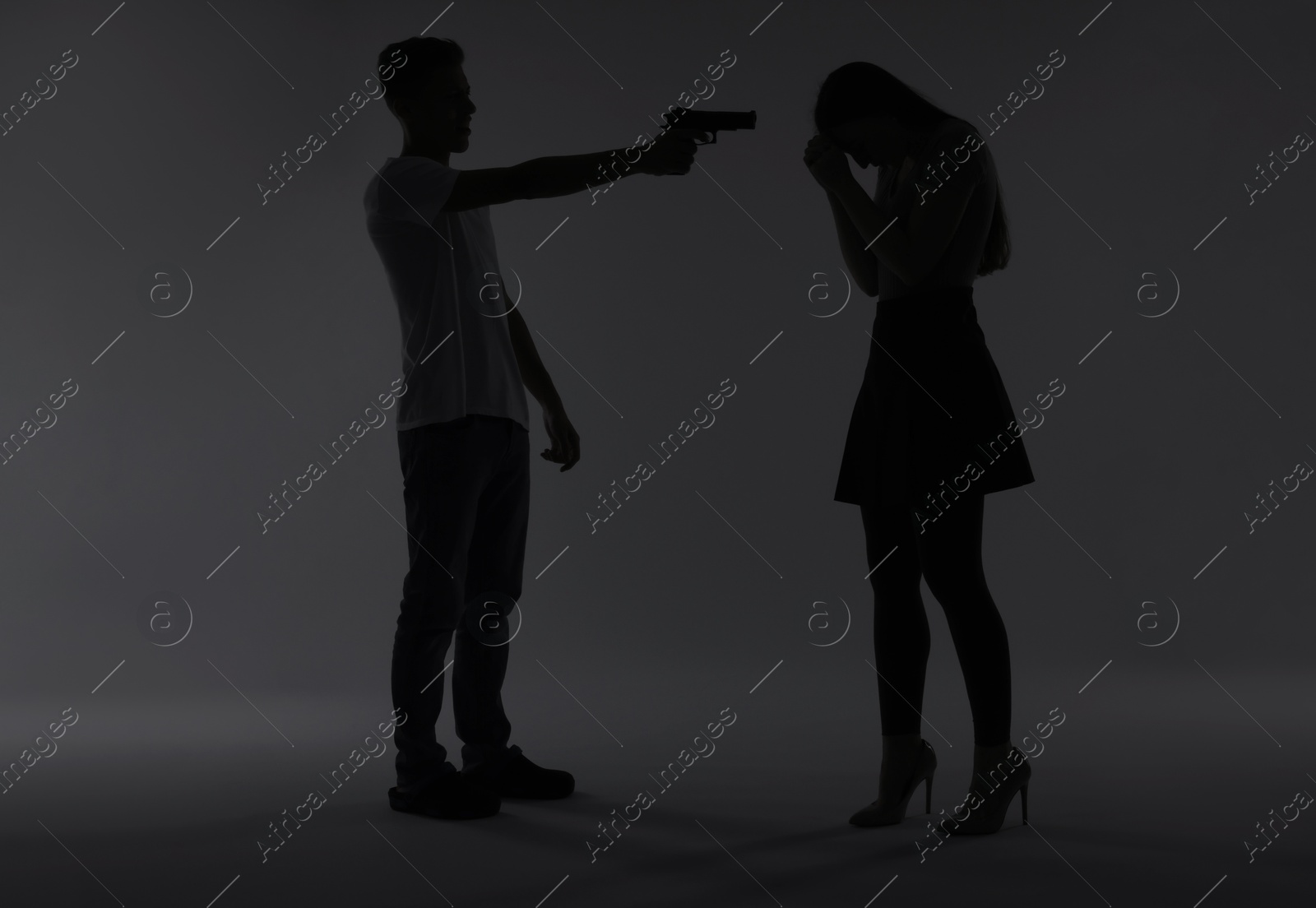 Photo of Domestic violence. Silhouette of man with gun threatening his wife on grey background