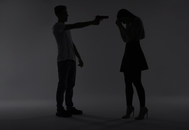 Photo of Domestic violence. Silhouette of man with gun threatening his wife on grey background