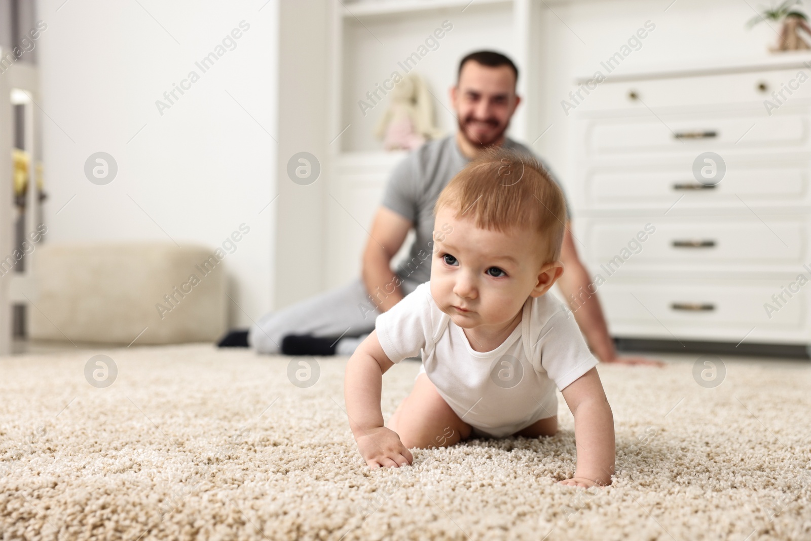 Photo of Father watching his little baby learning to crawl at home, selective focus