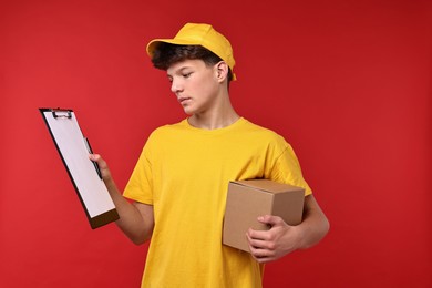 Photo of Teenage boy with parcel and clipboard working as courier on red background