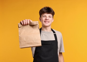 Photo of Teenage boy with paper bag working as cashier on orange background