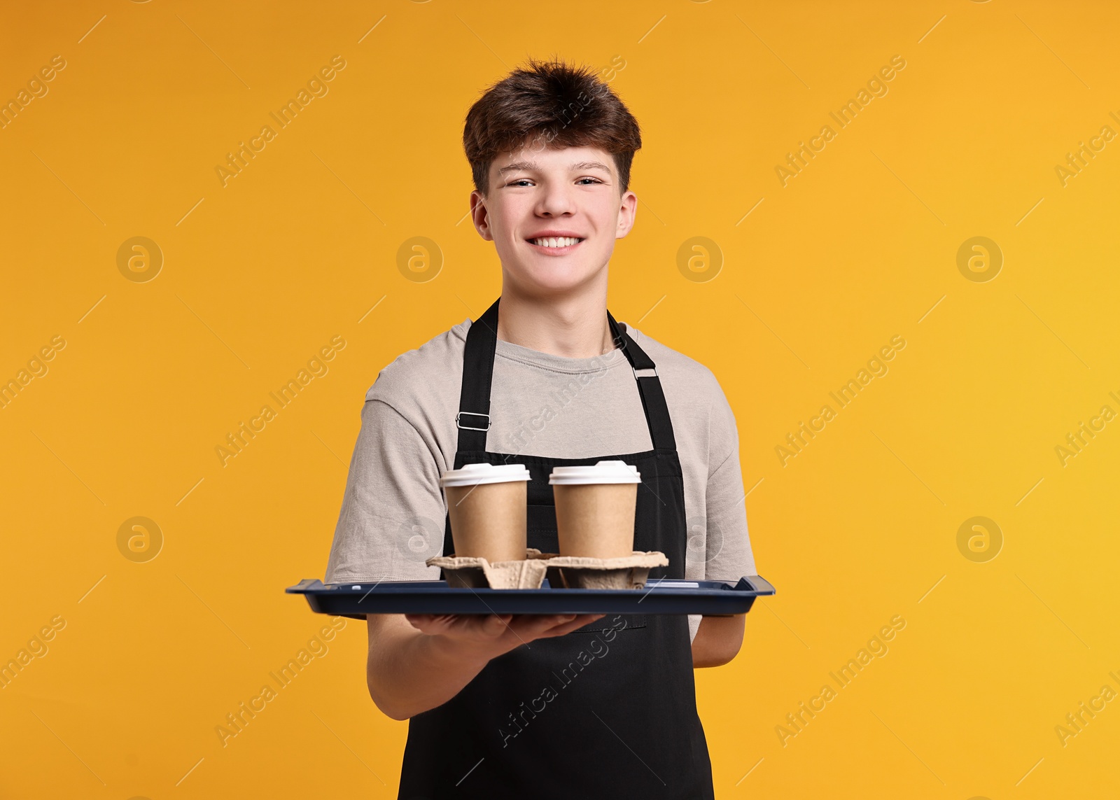 Photo of Teenage boy with order working as waiter on orange background