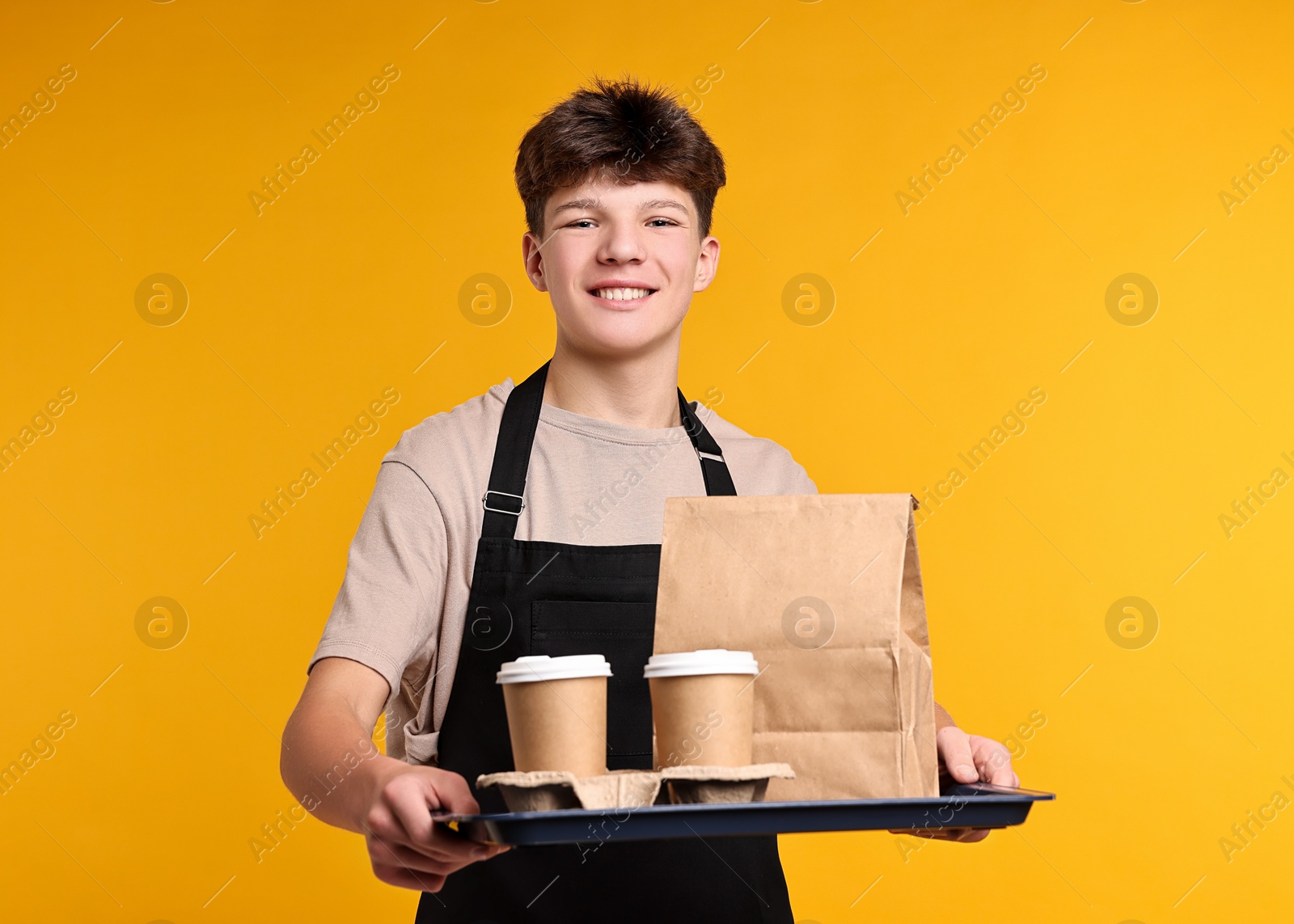 Photo of Teenage boy with order working as waiter on orange background