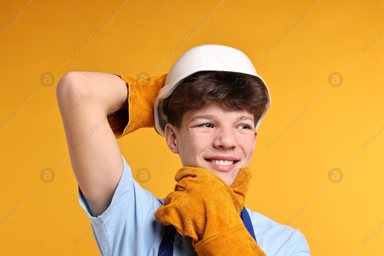 Photo of Teenage boy in hardhat working as builder on orange background