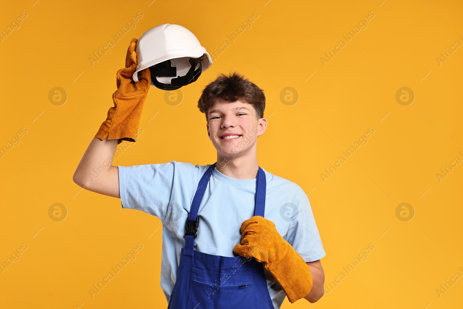 Photo of Teenage boy in hardhat working as builder on orange background