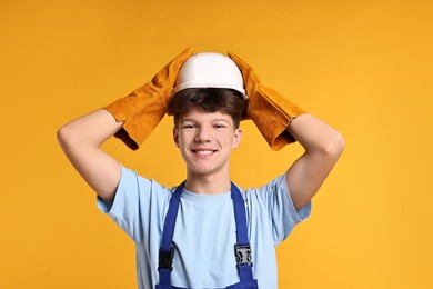 Photo of Teenage boy in hardhat working as builder on orange background