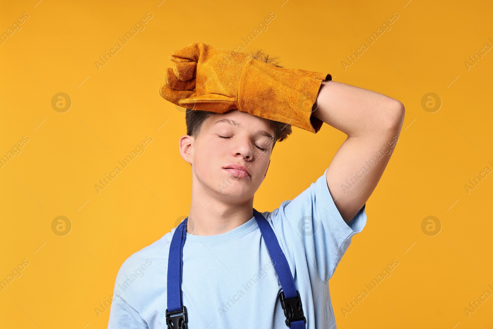 Photo of Teenage boy in protective gloves working as builder on orange background