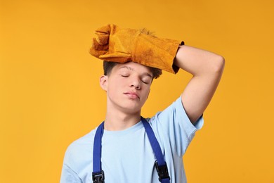 Photo of Teenage boy in protective gloves working as builder on orange background