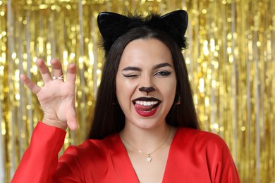 Playful woman with cat makeup and ears on golden background