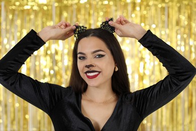 Photo of Beautiful woman with cat makeup and ears on golden background