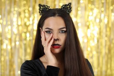 Photo of Beautiful woman with cat makeup and ears on golden background