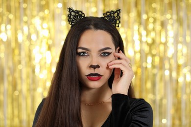 Photo of Beautiful woman with cat makeup and ears on golden background