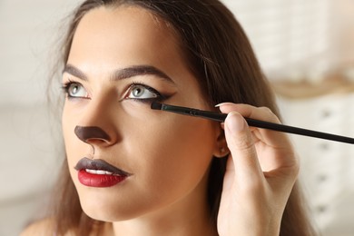 Artist doing cat makeup on woman's face indoors, closeup