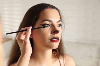 Photo of Artist doing cat makeup on woman's face indoors