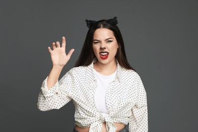 Playful woman with cat makeup and ears on grey background