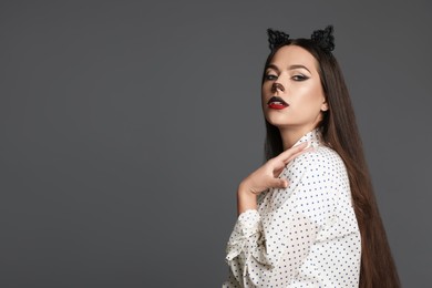 Photo of Attractive woman with cat makeup and ears on grey background. Space for text