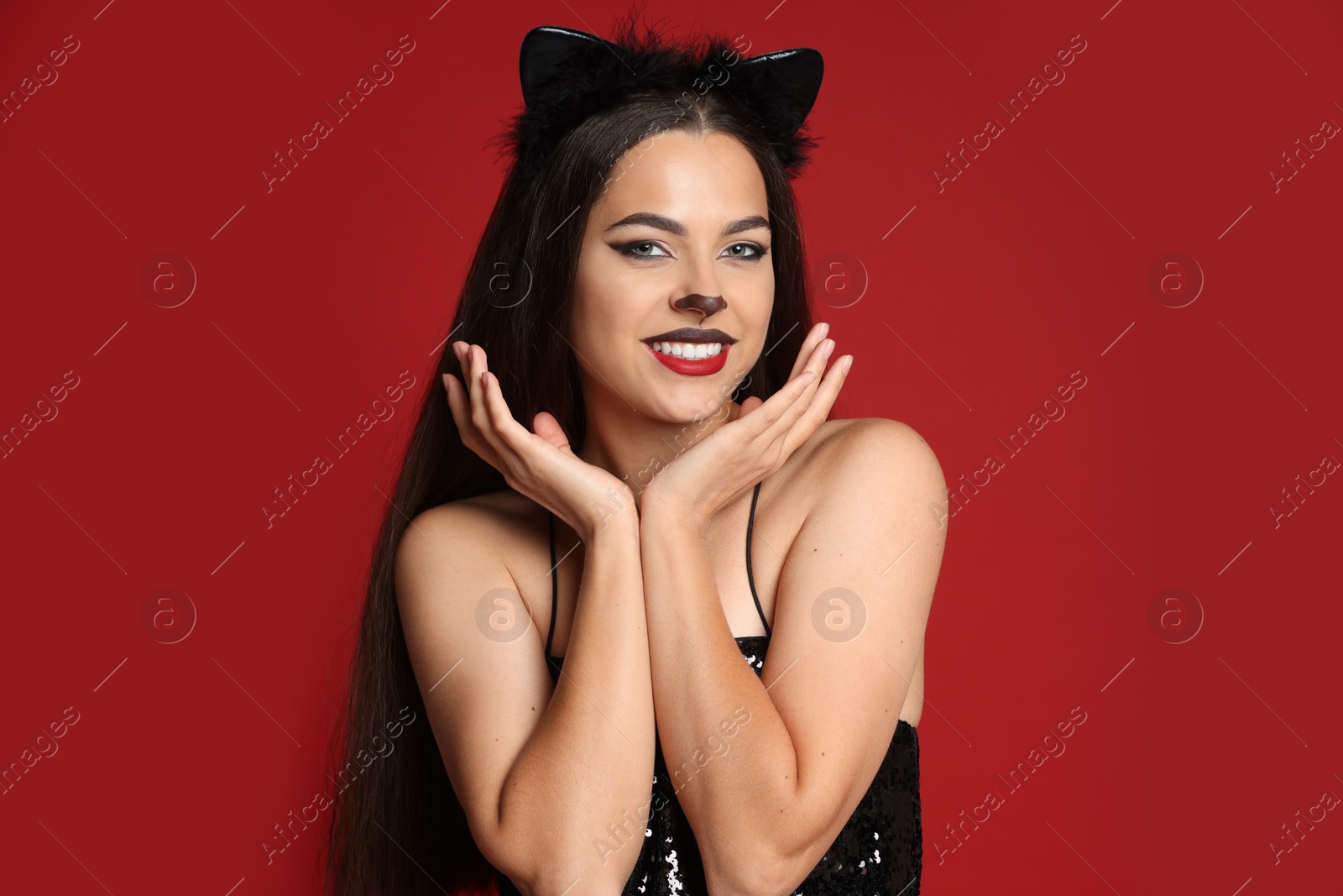 Photo of Beautiful woman with cat makeup and ears on red background