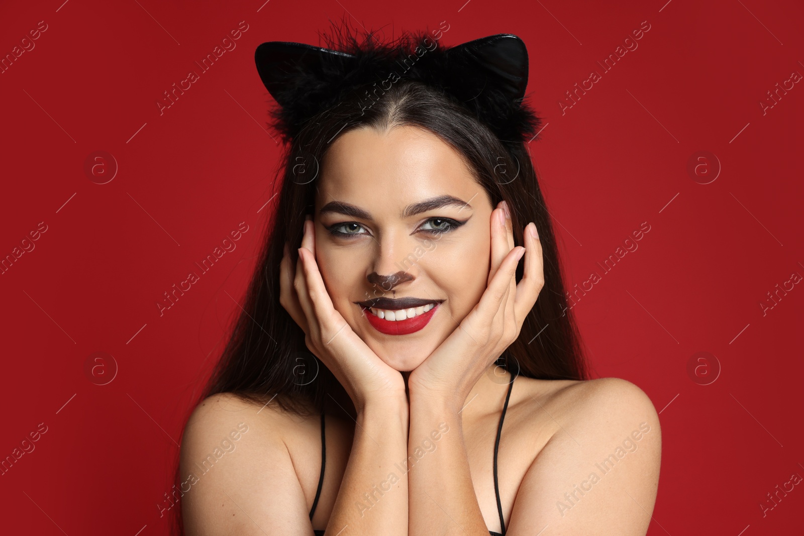 Photo of Beautiful woman with cat makeup and ears on red background