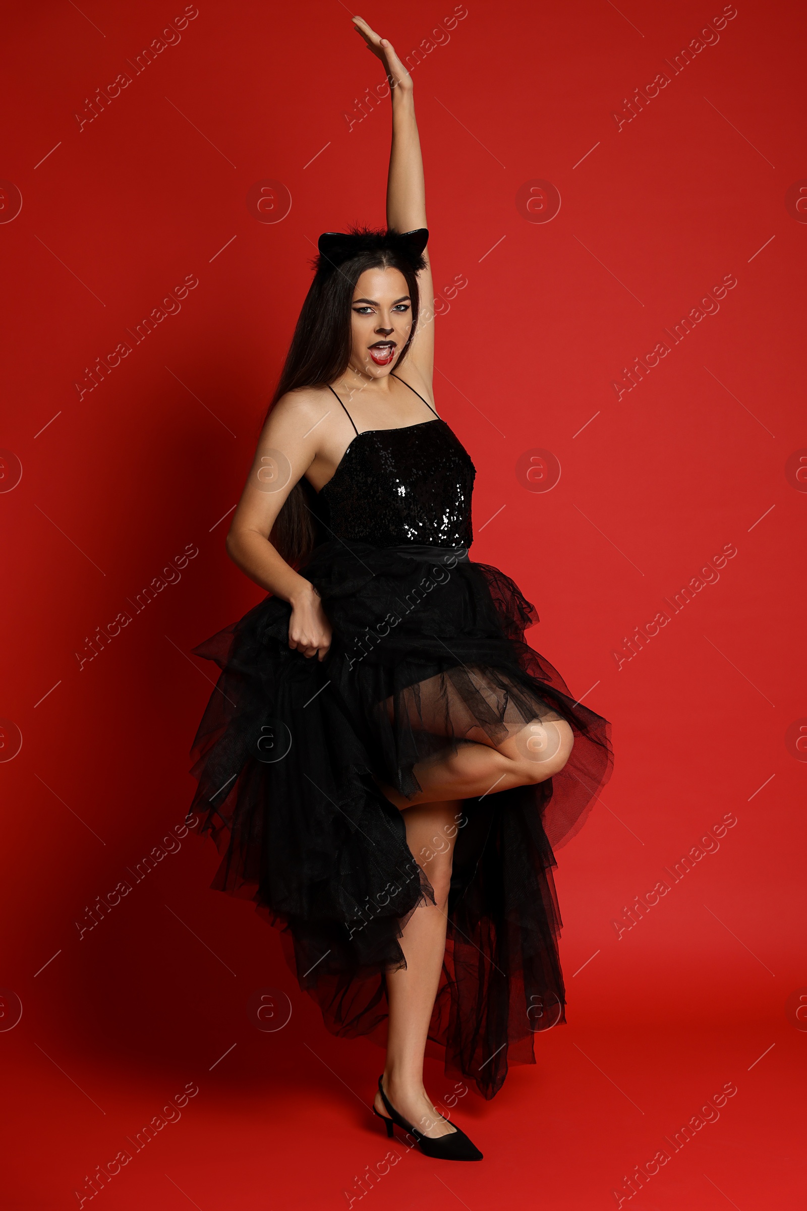 Photo of Woman with cat makeup and ears in beautiful dress on red background