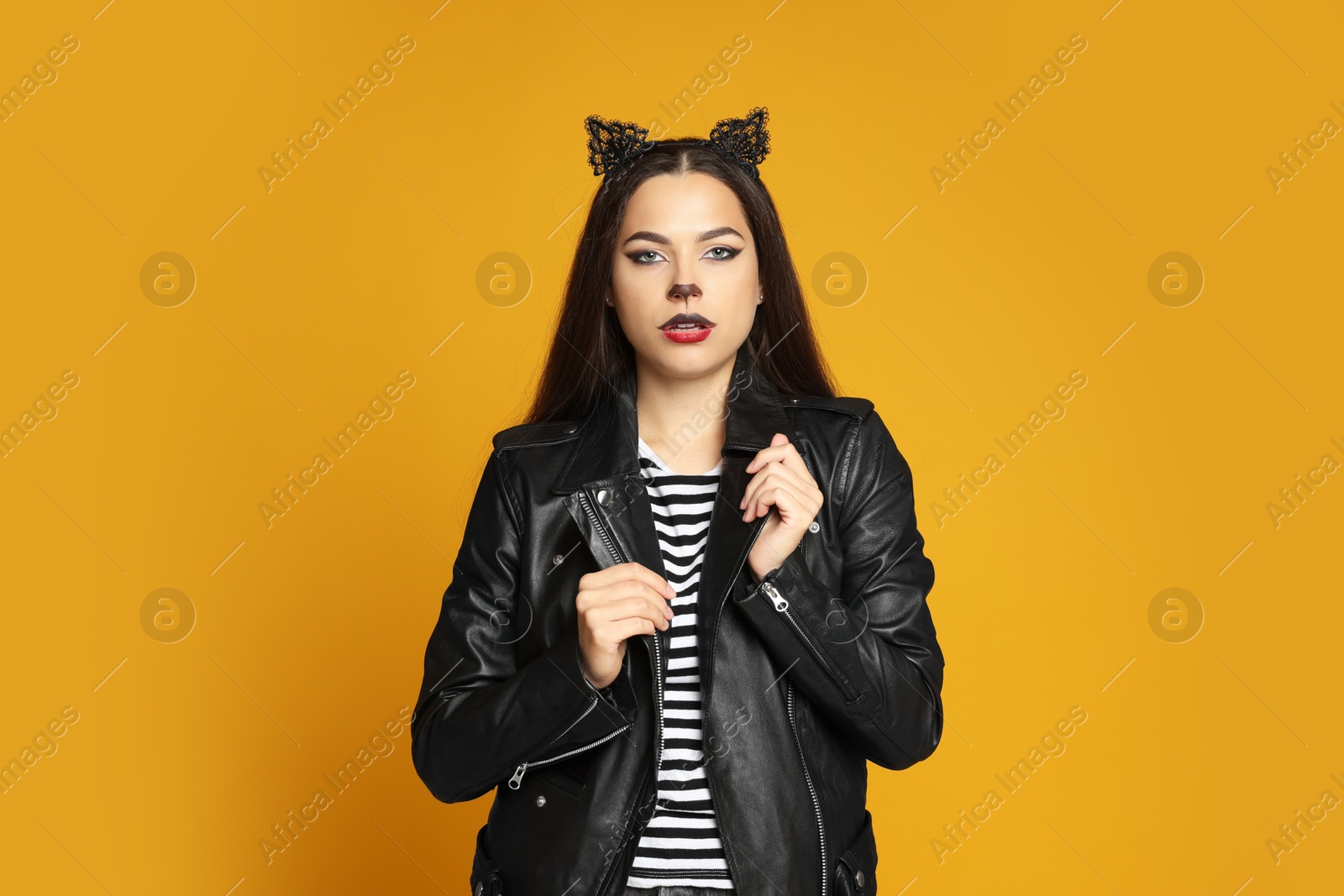 Photo of Woman with cat makeup and ears in leather jacket on orange background