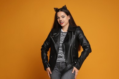 Photo of Woman with cat makeup and ears in leather jacket on orange background