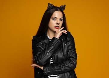 Photo of Woman with cat makeup and ears in leather jacket on orange background