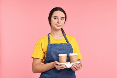 Photo of Girl in apron with takeaway paper cups of coffee on pink background. Work for teenagers