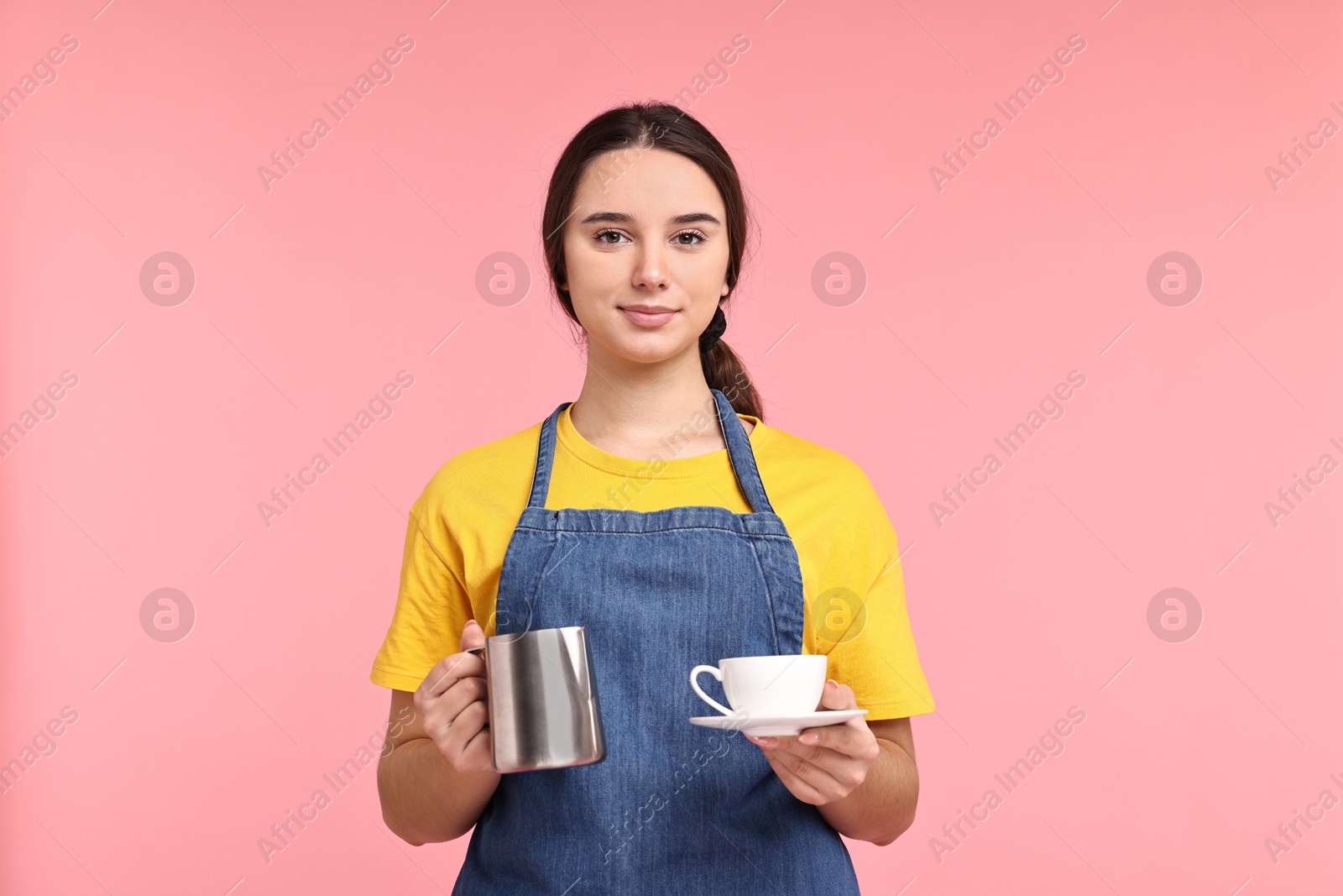 Photo of Girl in apron with pitcher and cup of coffee on pink background. Work for teenagers