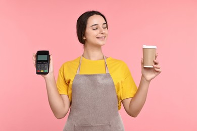 Photo of Girl in apron with paper cup of coffee and payment terminal on pink background. Work for teenagers