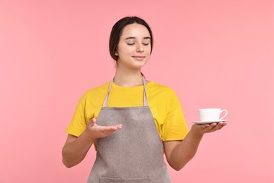 Photo of Girl in apron with cup of coffee on pink background. Work for teenagers