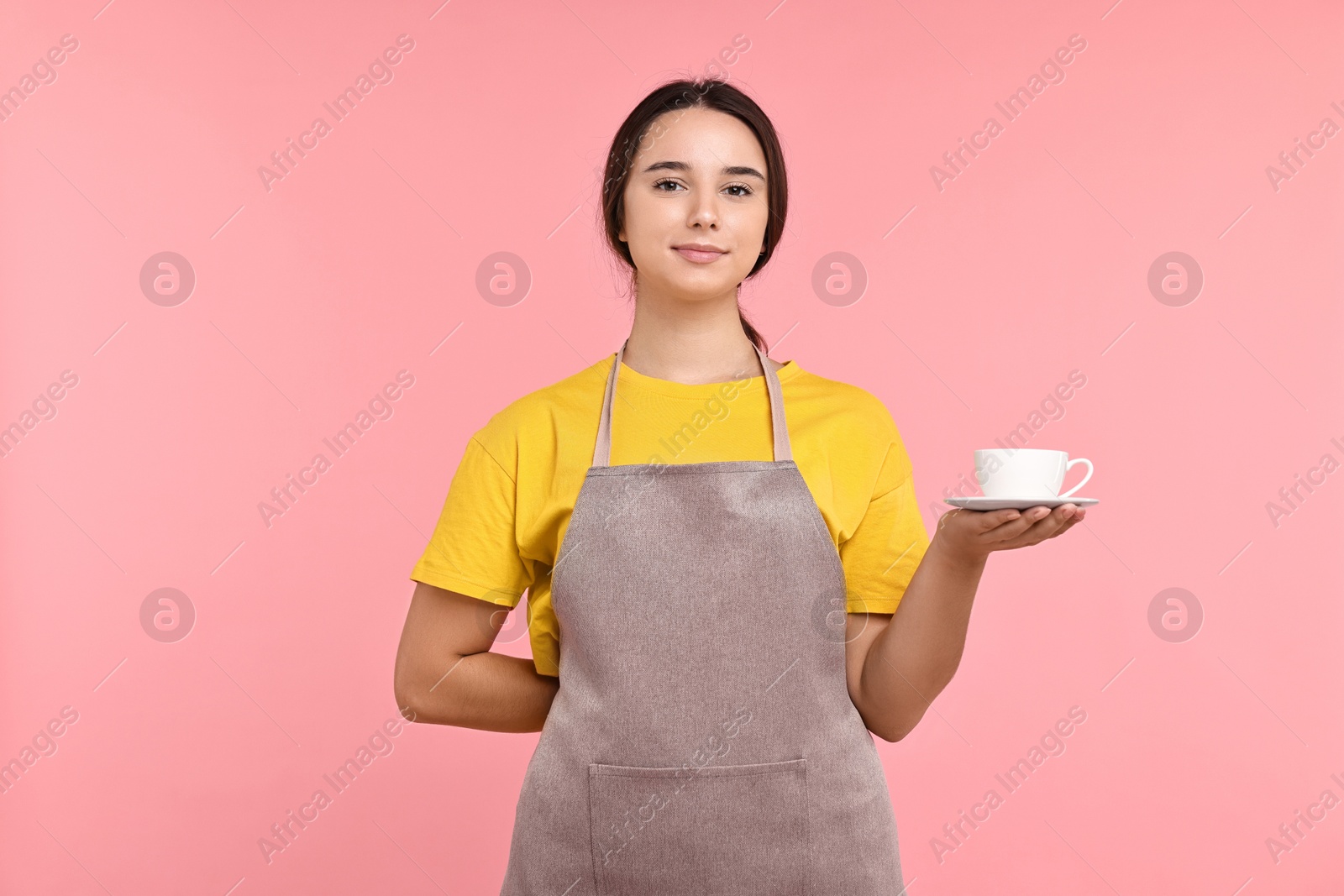 Photo of Girl in apron with cup of coffee on pink background. Work for teenagers